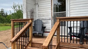 Una terraza de madera con una escalera que lleva a una casa de fachada blanca.