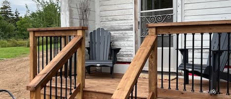 Um deck de madeira com uma escadaria que leva a uma casa com fachada branca.