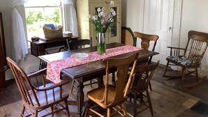 Comedor con mesa de madera, seis sillas, un jarrón con flores y una ventana con cortinas.