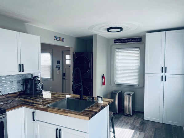 Une cuisine moderne avec des meubles blancs, un plan de travail en bois, des appareils en acier inoxydable et un panneau indiquant : « Bonne nourriture, bons amis, bons moments. »