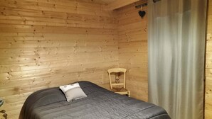 En stuga med träpanel, inredd med en säng, en stol och en gardin.