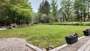 Ett grönområde utomhus med en träbänk, en eldstad och blomlådor.