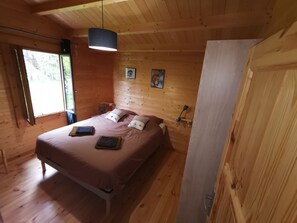 A wooden room with a bed, a hanging light fixture, and a window.