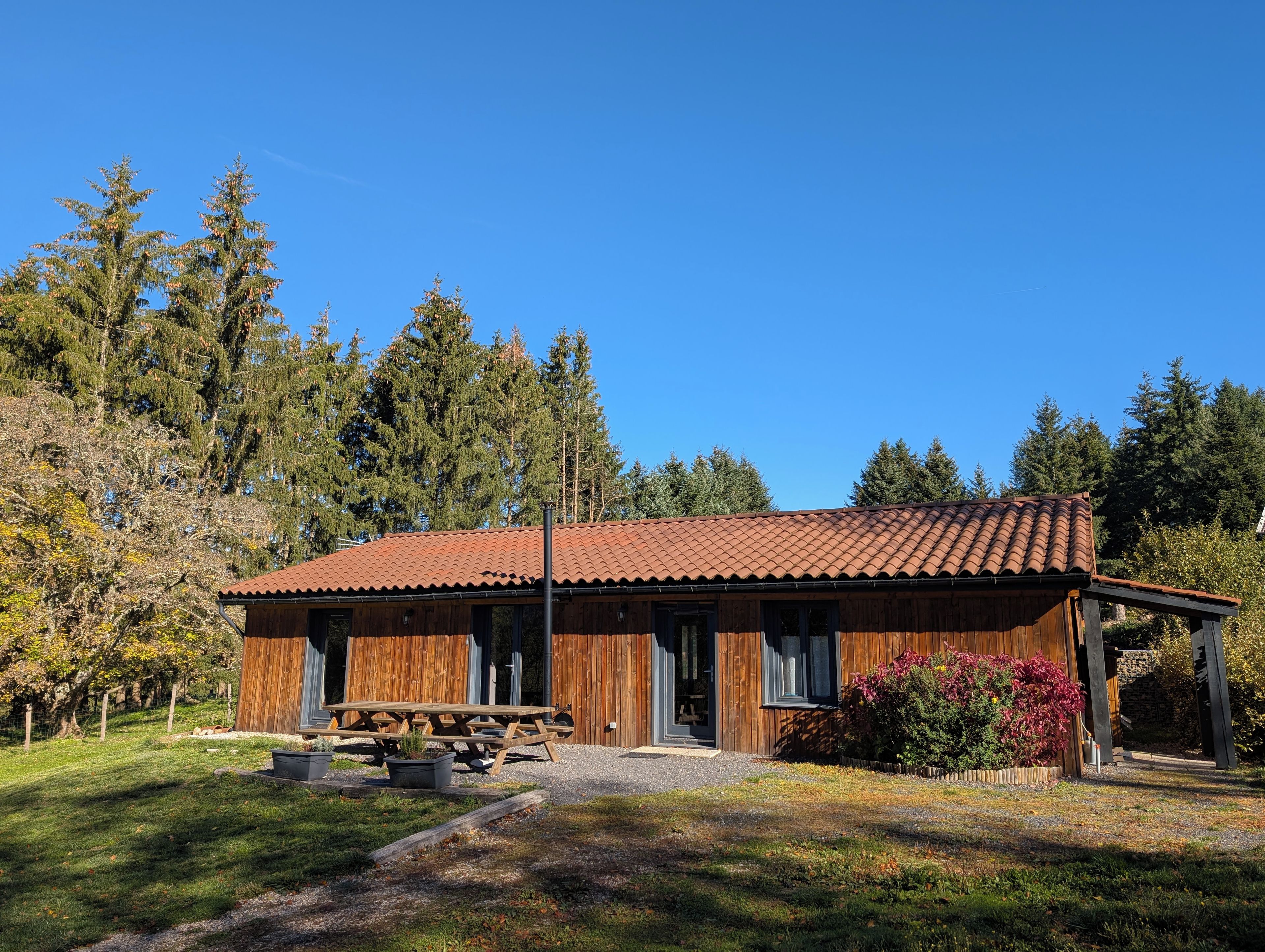 A wooden cabin with a tiled roof, a picnic table, and a gravel driveway.