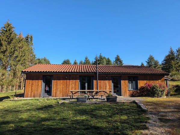 A wooden cabin with a tiled roof, a picnic table, and a small garden area.