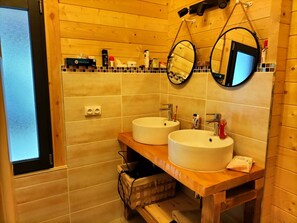 A wooden bathroom with two sinks, a mirror, and a shelf with toiletries.