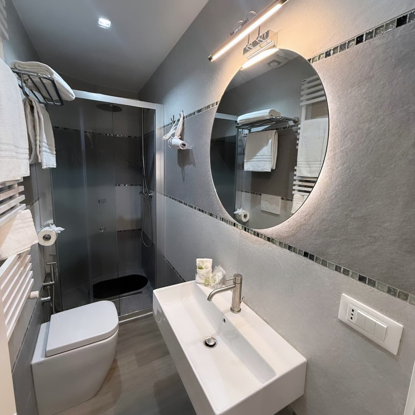 Un baño moderno con cabina de ducha, inodoro, lavabo y espejo con marco circular.