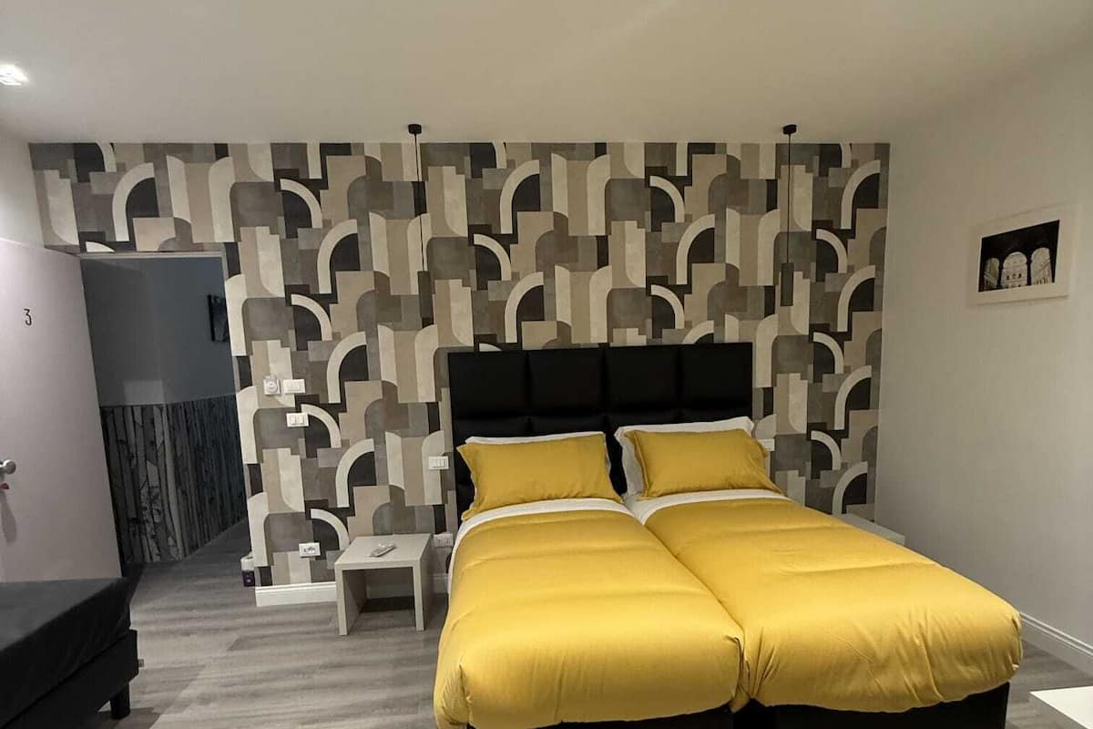 A modern bedroom with a large bed, a nightstand, and a wall with a geometric pattern.
