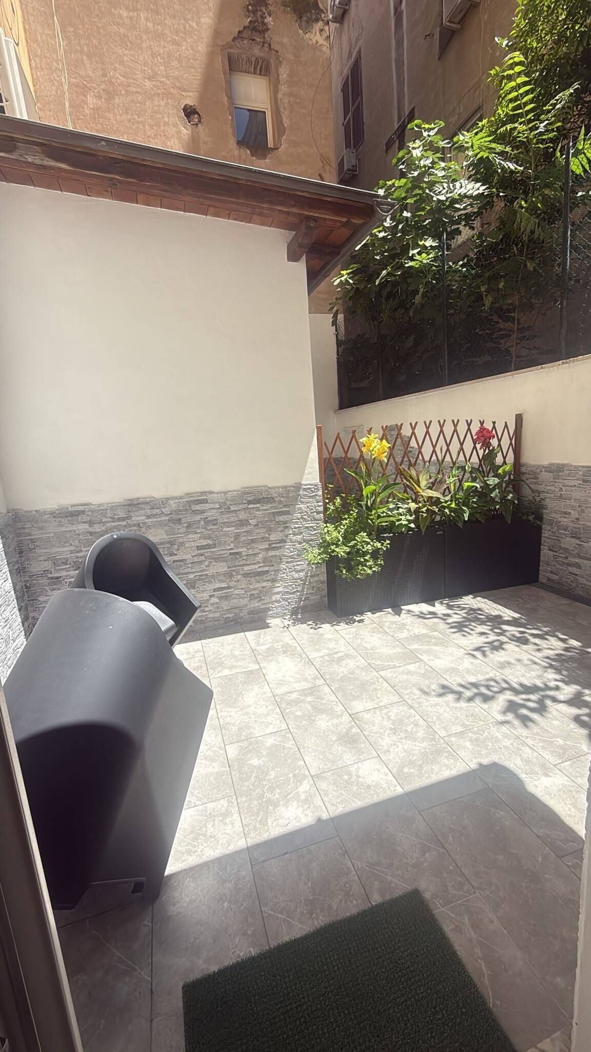 A patio with a table and chairs, a planter with flowers, and a stone wall.