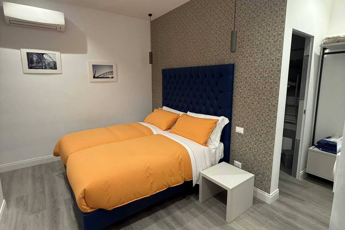 A modern bedroom with a double bed, a bedside table, a wardrobe, and a patterned wall.