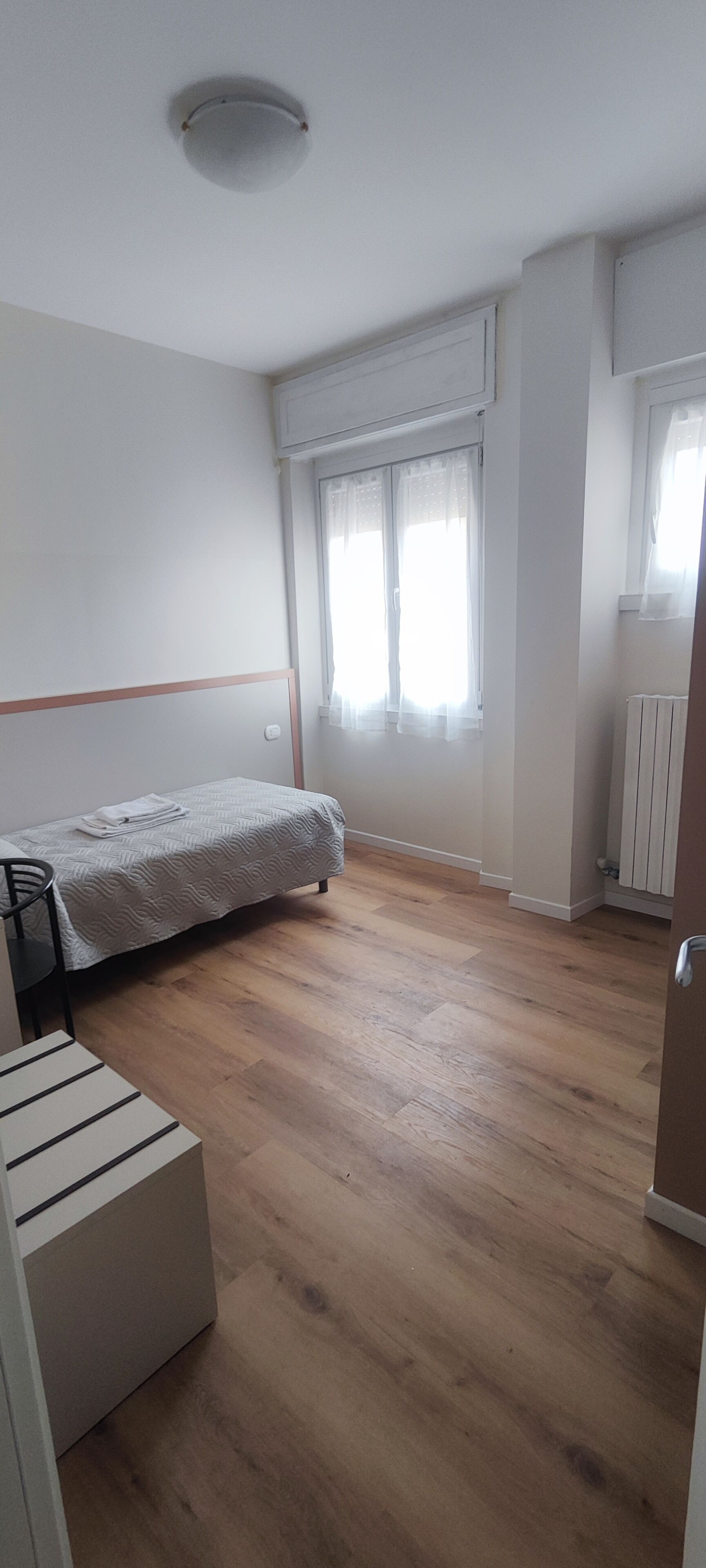 Ein Zimmer mit einem Bett, einem Sessel, einer Heizung und einem Fenster mit Vorhängen.