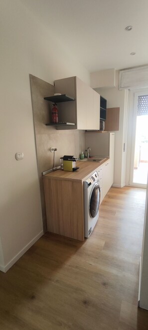 A compact kitchen with a washing machine, a small countertop, and a built-in oven. - Vroom509 (Verona)