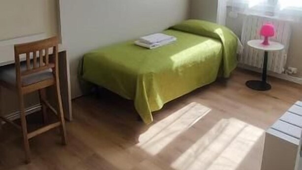 A room with a bed, a chair, a small table, and a window with curtains. - Vroom509 (Verona)
