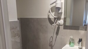 A bathroom with a toilet, a sink, a mirror, and a hairdryer mounted on the wall. - Vroom509 (Verona)