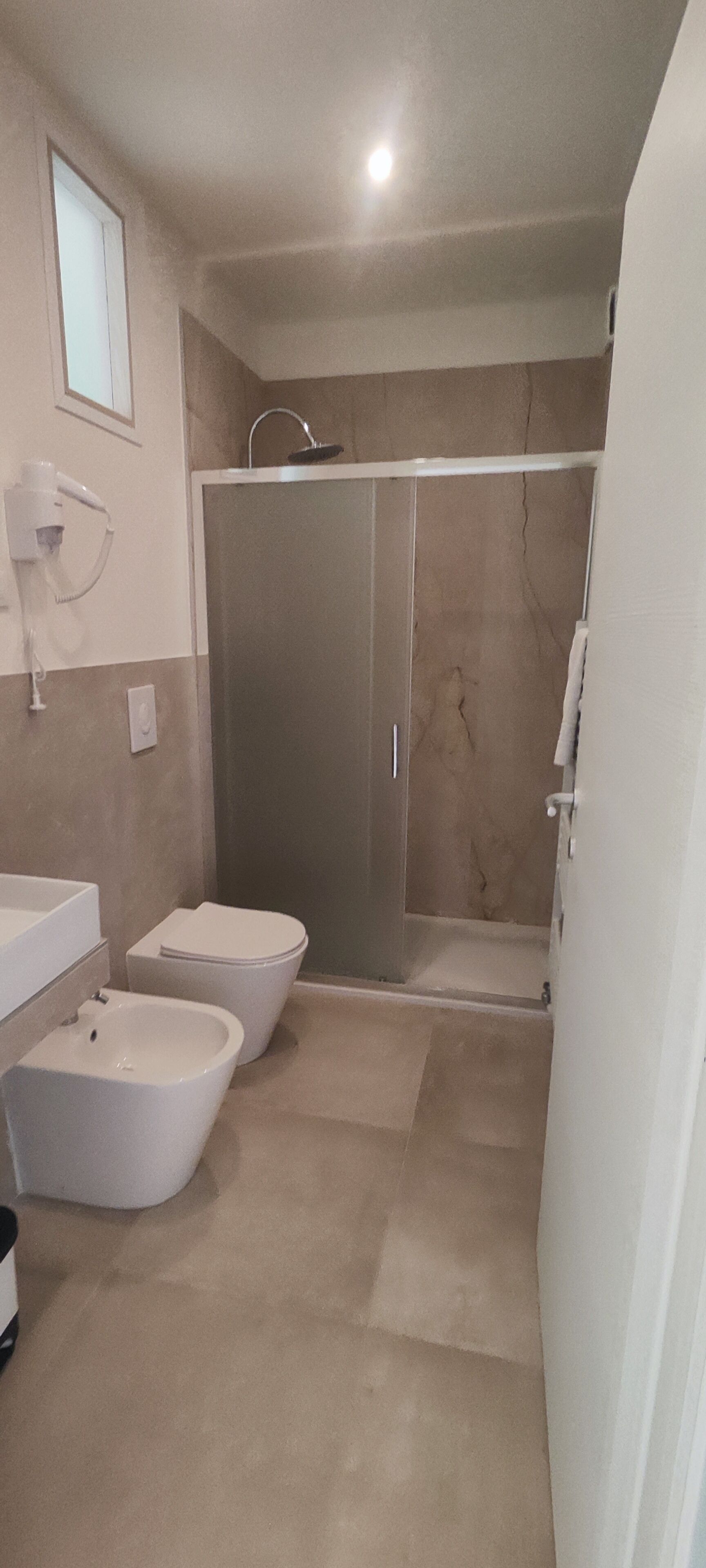 A bathroom with a shower, two toilets, a bidet, and a sink.