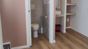 A room with a wooden floor, a white door leading to a bathroom, and a white wall. - Vroom509 (Verona)