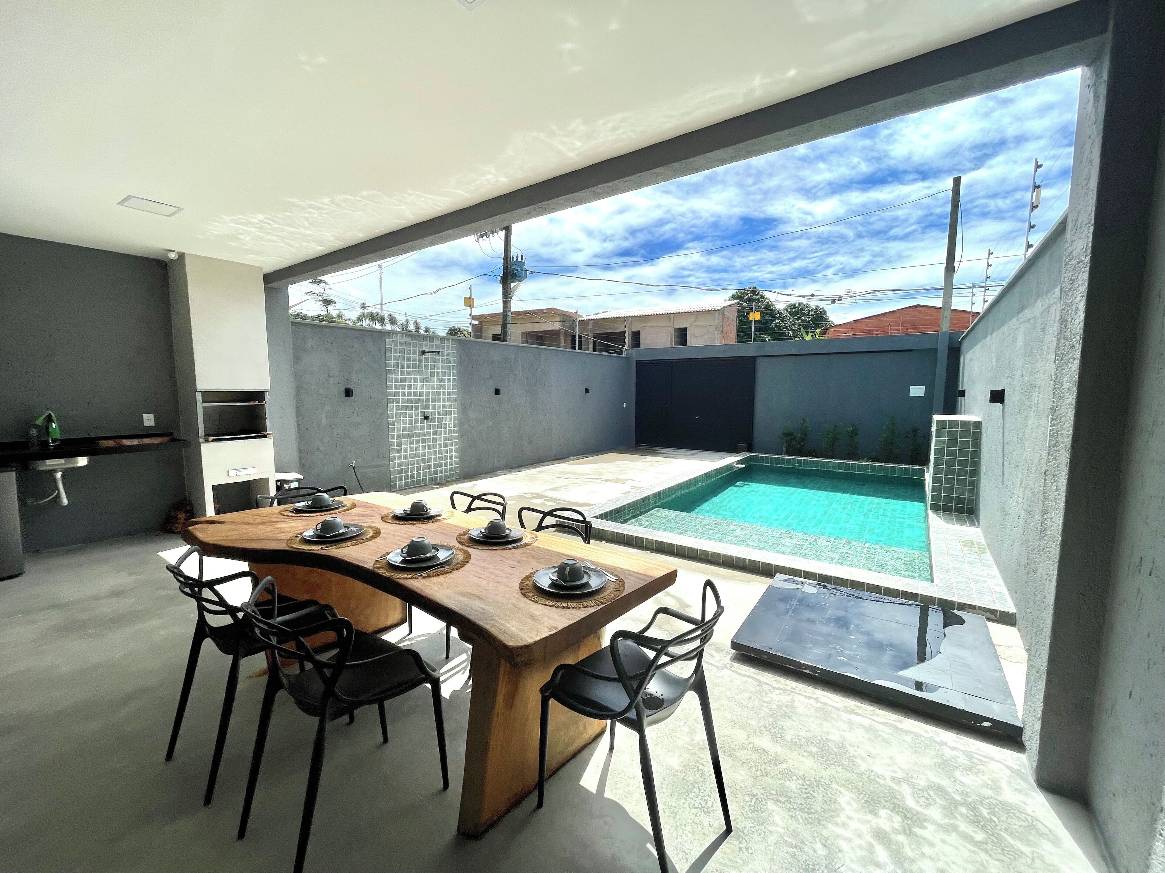 A modern outdoor dining area with a pool, a kitchen, and a view of the neighborhood.