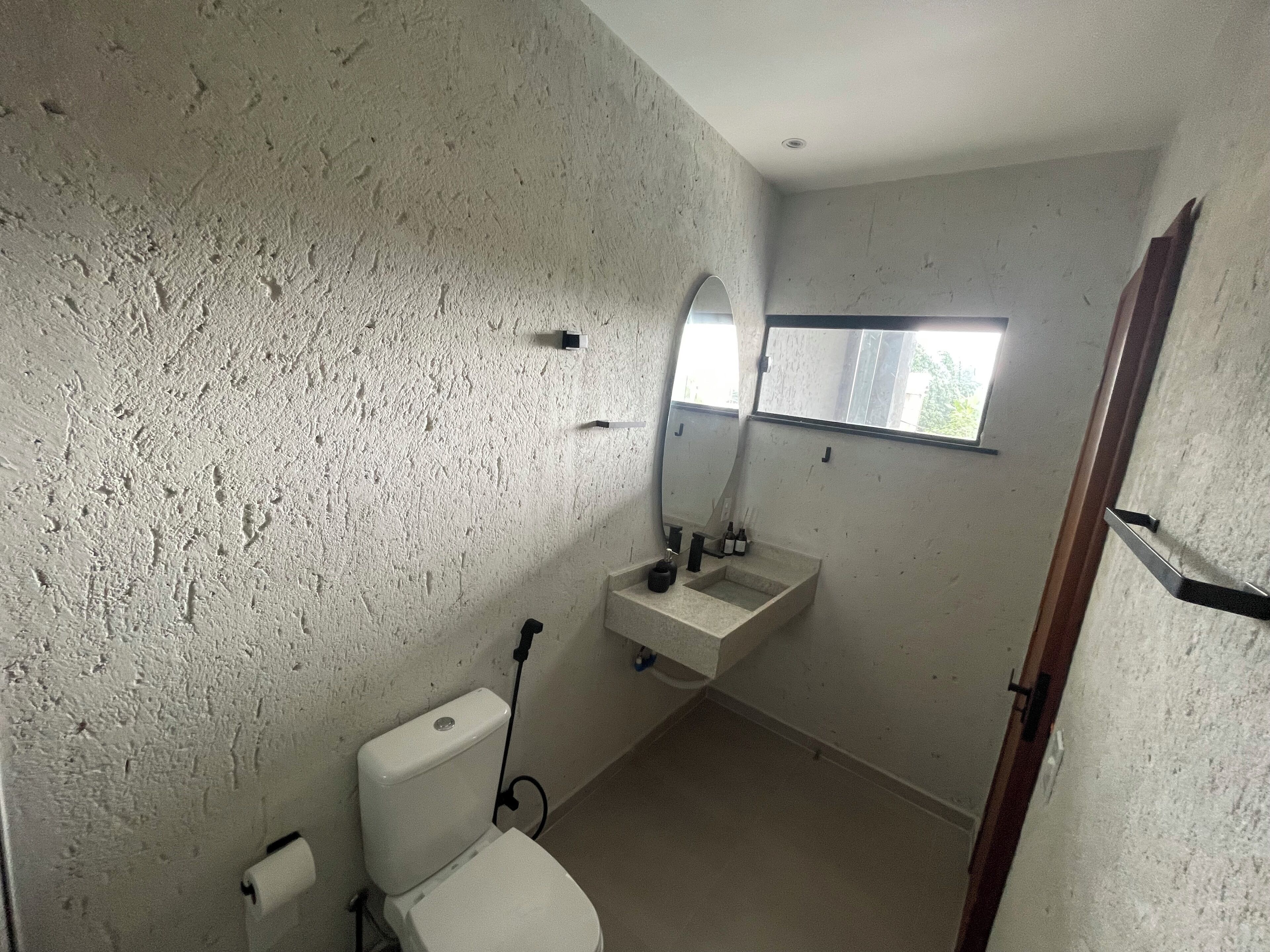 Un baño pequeño con pared texturizada, inodoro, lavamanos, espejo y ventana.