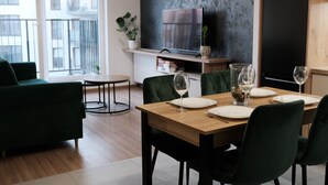 A modern dining area with a wooden table set for four, green upholstered chairs, and a television mounted on a black wall. - Apartments Space and More - Apartamenty Wrocław (Wrocław)