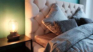 A bedroom with a tufted headboard, a bedside lamp, and a bed with striped bedding. - Apartments Space and More - Apartamenty Wrocław (Wrocław)
