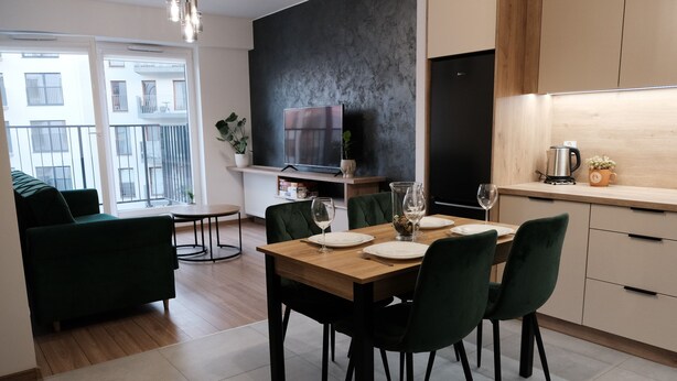 A modern dining area with a wooden table, green chairs, and a TV mounted on the wall. - Apartments Space and More - Apartamenty Wrocław (Wrocław)