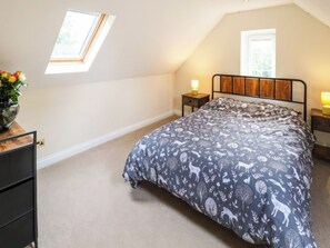 A bedroom with a sloped ceiling, a skylight, a bed with a patterned duvet, bedside tables with lamps, and a small wooden nightstand.