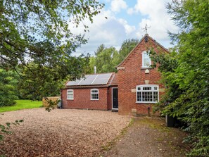 A brick house with a sloped roof, solar panels, and a gravel driveway.