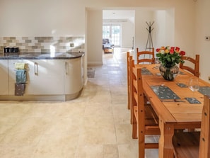 Una cocina moderna con una isla curva, un comedor con sillas de madera y una mesa preparada para dos personas, y un jarrón con flores sobre la mesa.