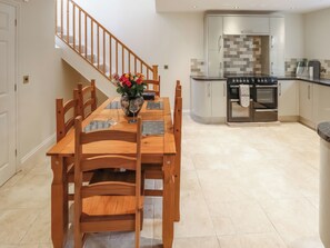 A dining area with a wooden table set for four, a vase with flowers, and a kitchen in the background with a stainless steel refrigerator and oven. - 1 bedroom accommodation in Frithville, near Lincolnshire (Frithville, near Lincolnshire)