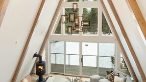 Quarto de loft aconchegante com teto inclinado, janelas amplas, lareira e lustre moderno.