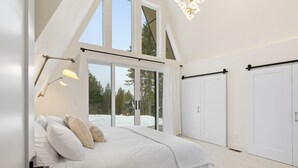 Quarto com cama grande, portas de vidro deslizantes para área externa coberta de neve e lustre.