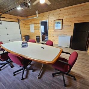 A conference room with a long table, red chairs, a projector, and a refrigerator.