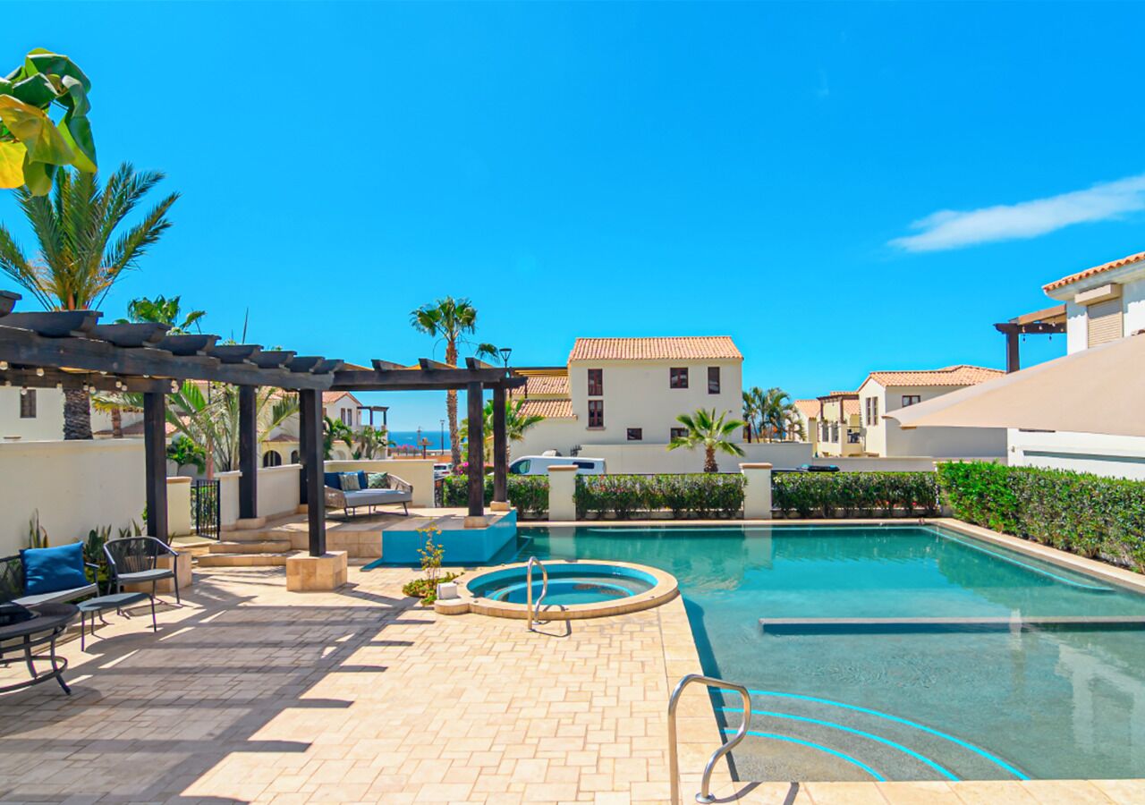 A pool area with a hot tub, lounge chairs, and a pergola.