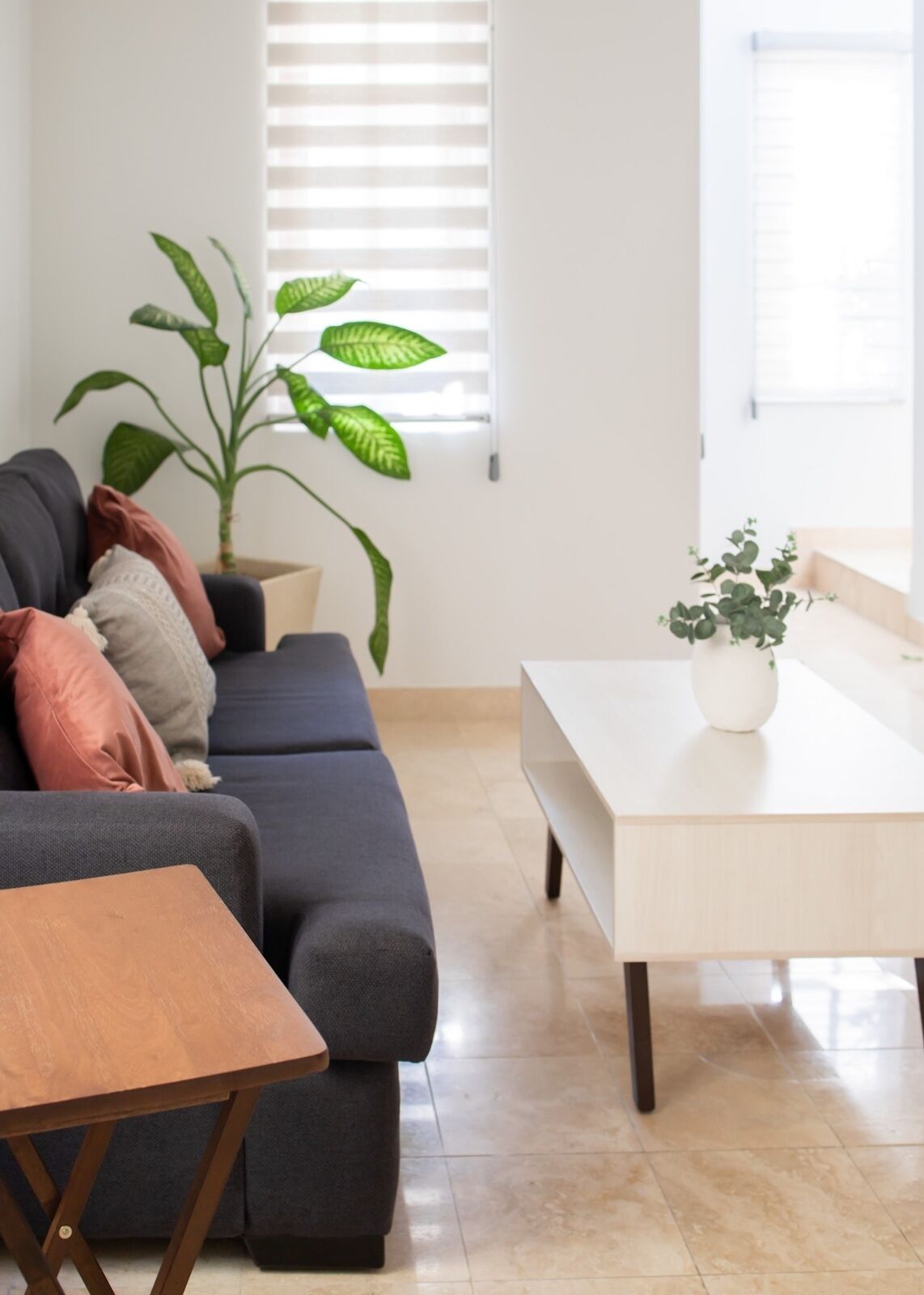 Una sala moderna con un sofá gris oscuro, una mesa de centro de madera, una mesa de comedor blanca y una planta en maceta.