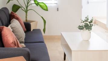 Una sala moderna con un sofá gris oscuro, una mesa de centro de madera, una mesa de comedor blanca y una planta en maceta.
