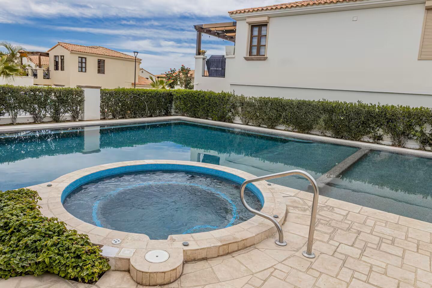 Piscina com hidromassagem, cercada por um terraço de tijolos e vegetação.