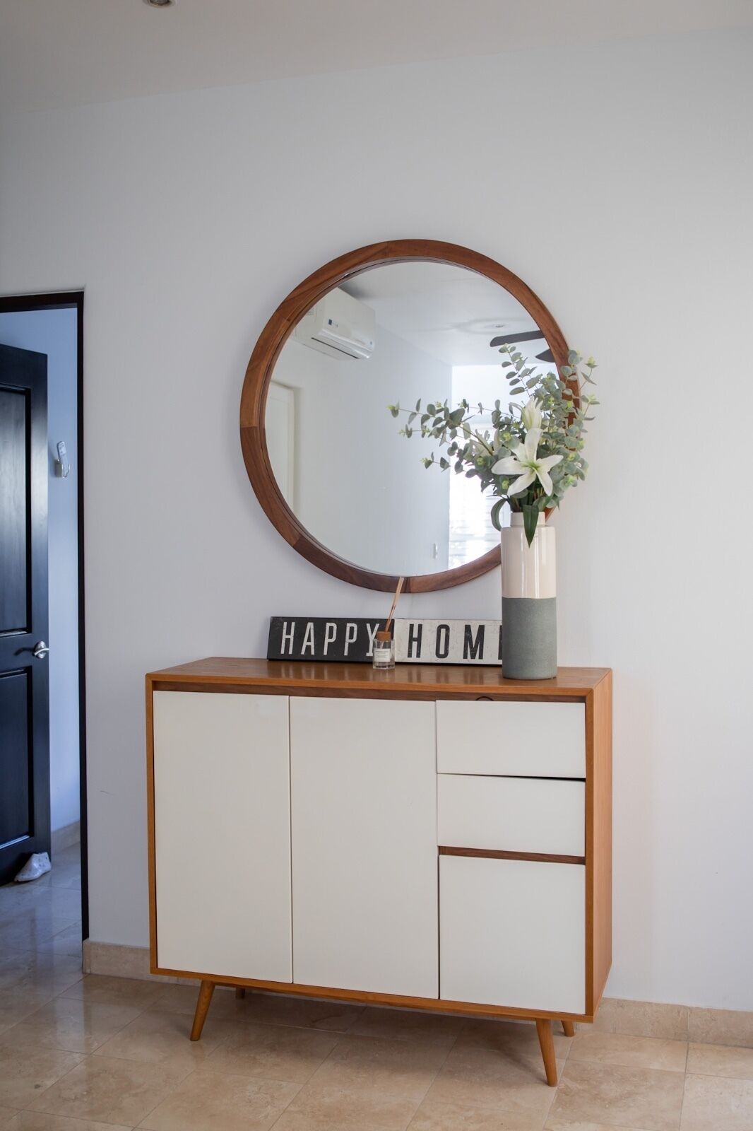 A white cabinet with a wooden frame, a round mirror, and a sign that reads "HAPPY HOME" above it.