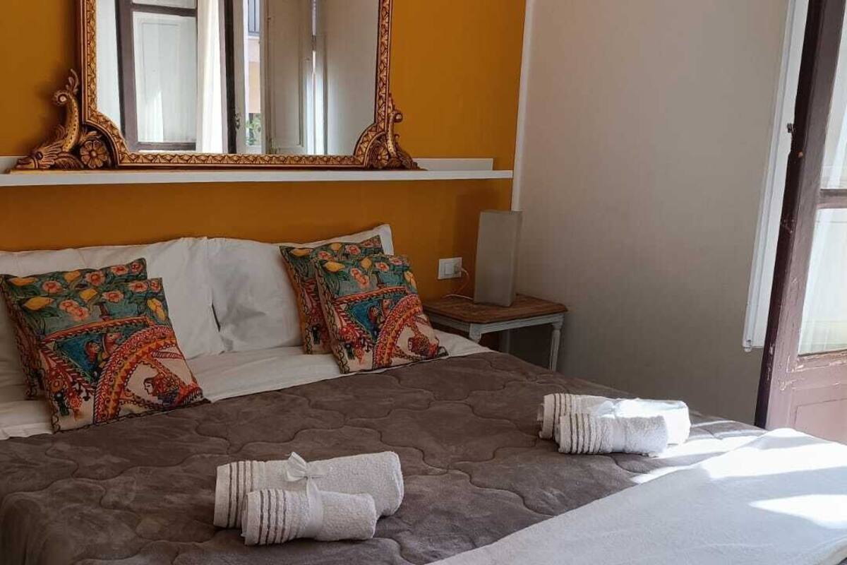 A neatly made bed with patterned pillows, a bedside table with a lamp, and a large mirror above the bed.
