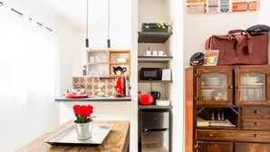 Ett kompakt kök med mikrovågsugn, kaffebryggare och ett litet kylskåp. Det finns ett träbord med en vas med röda blommor och ett bricka. Ett skåp med glasdörrar syns till höger.