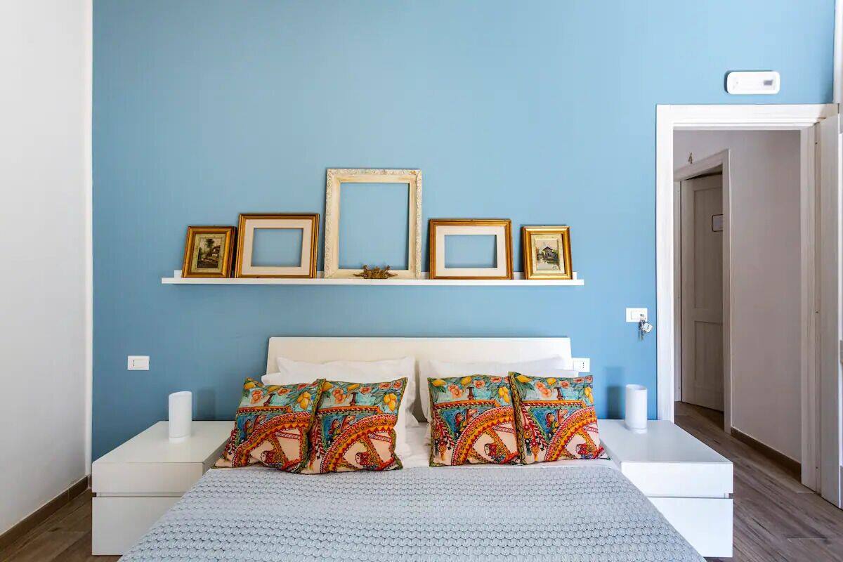 A bedroom with a blue wall, white bed, and decorative pillows.