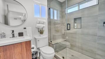 Een moderne badkamer met een douchecabine van glas, een wit toilet, een wastafel met spiegel en een badmeubel met houten kastje.