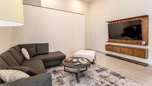 A modern living room with a sectional sofa, a small ottoman, a coffee table, and a flat-screen TV mounted on a wooden panel.