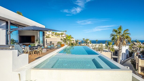 A rooftop infinity pool with a clear view of the ocean, surrounded by palm trees and modern outdoor seating.