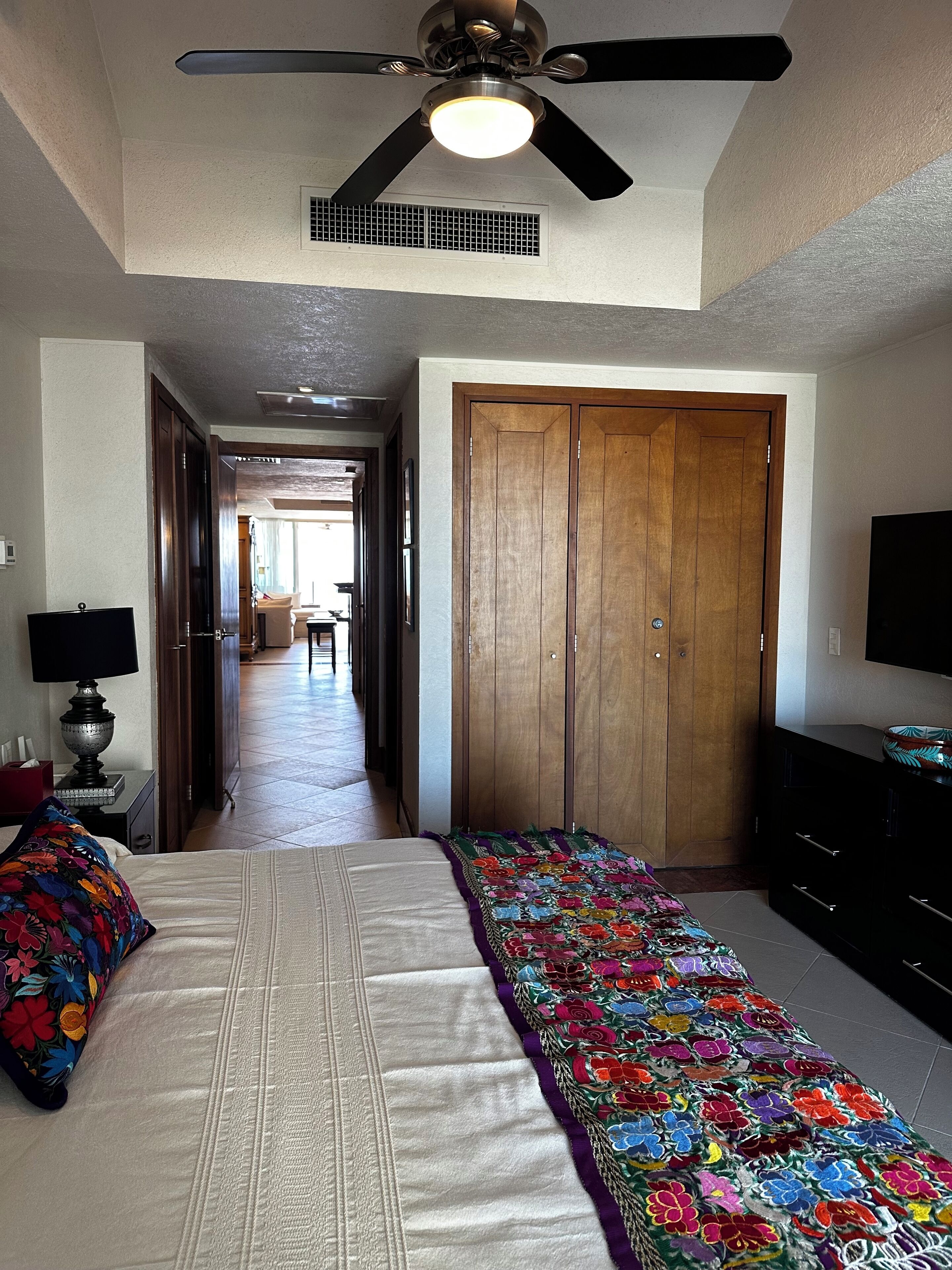 A bedroom with a bed, a ceiling fan, a wooden wardrobe, and a television.