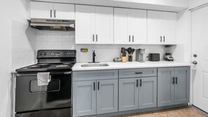 A modern kitchen with white cabinets, a black stove, a sink, and various kitchen appliances. - Budget-Friendly Apt | WD, Wifi & Modern Amenities (Paterson)