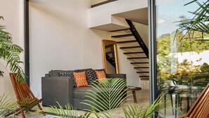 A modern living room with a grey sofa, wooden chairs, and a staircase. - Mistiq Luxury Condo Min. from Everything (Tulum)