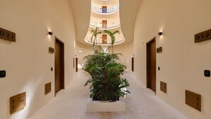 A hotel corridor with a central planter, multiple floors, and numbered doors. - Mistiq Luxury Condo Min. from Everything (Tulum)