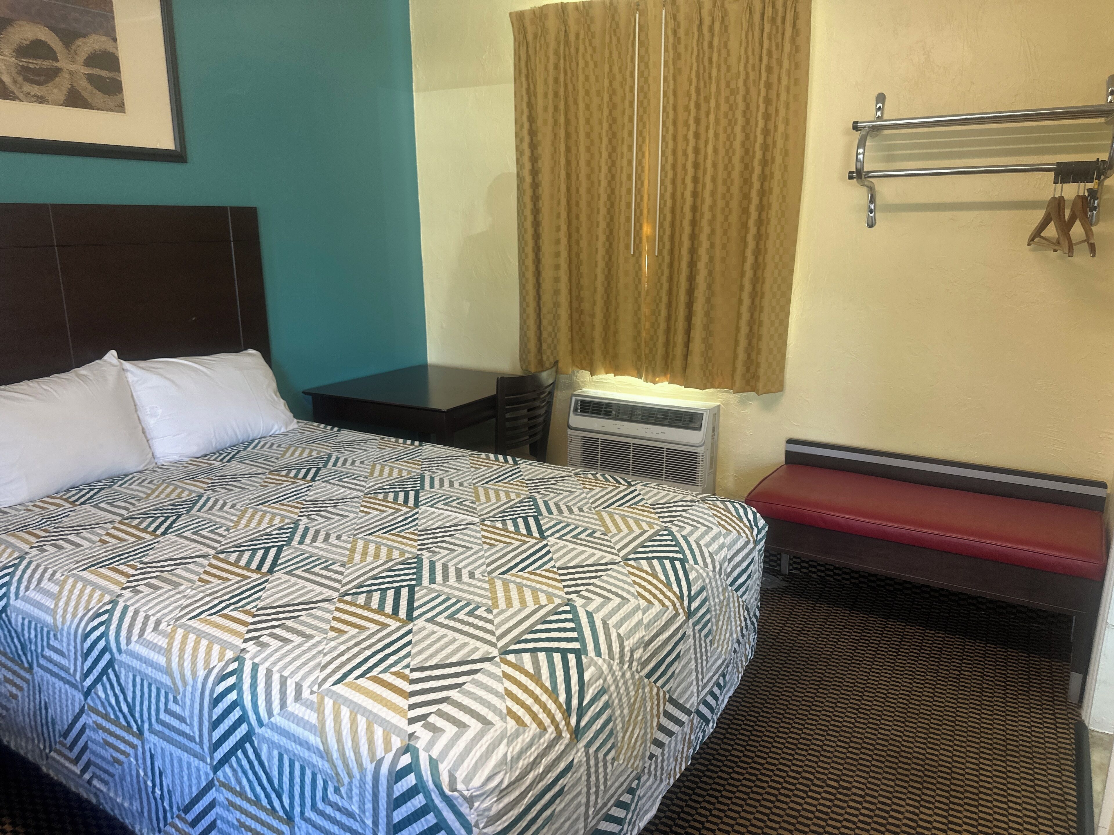 Une chambre d’hôtel avec un grand lit, une petite table, un climatiseur, un banc et un rideau.
