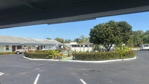 A parking lot with a building that has a flat roof and a sign indicating no smoking. There are several cars parked, and a tree is visible in the foreground. - Tropical Palm Motel (North Fort Myers)