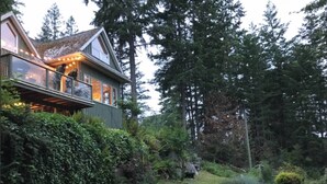 A house with a glass balcony overlooking a garden with various plants and a stone wall.